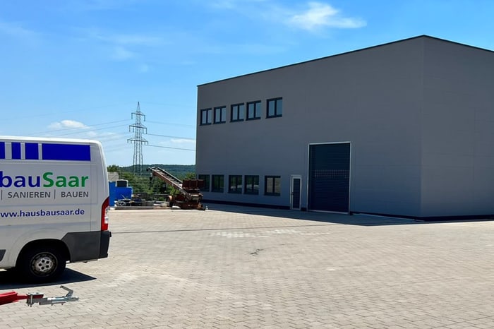 Weißer Transporter mit Schilder und T. KNÖBL Dachdeckerei Logo vor grauem Firmengebäude.